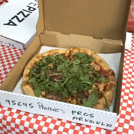 Paninis pizza box opening to show a large pizza covered in arugula