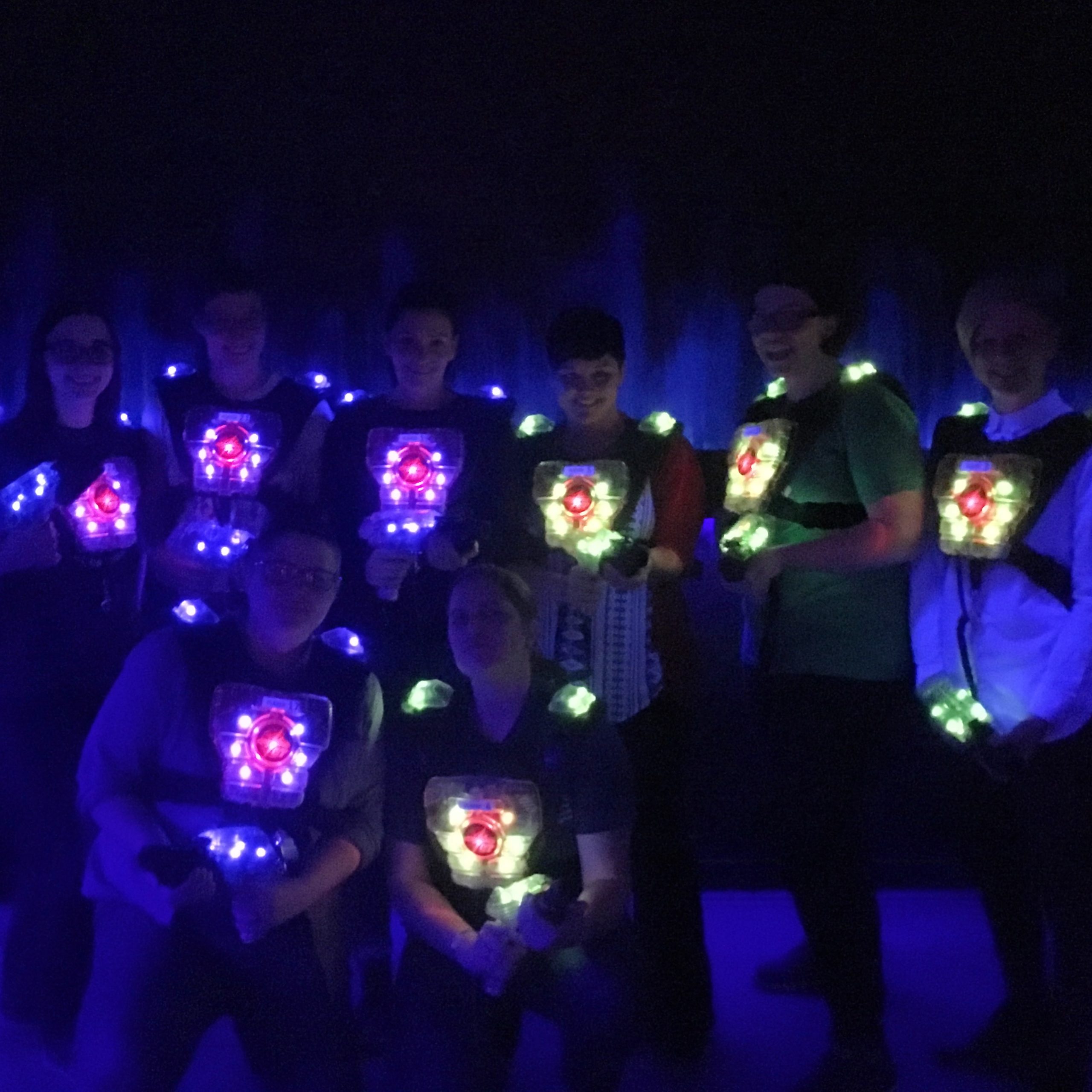 Kick Point team playing laser tag, illuminated by their glowing vests and laser guns in a dark room
