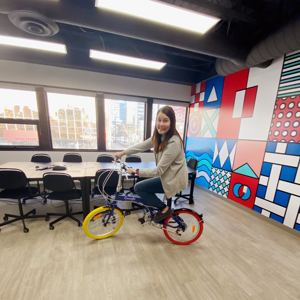 Jen rides a Google bike around the Kick Point boardroom
