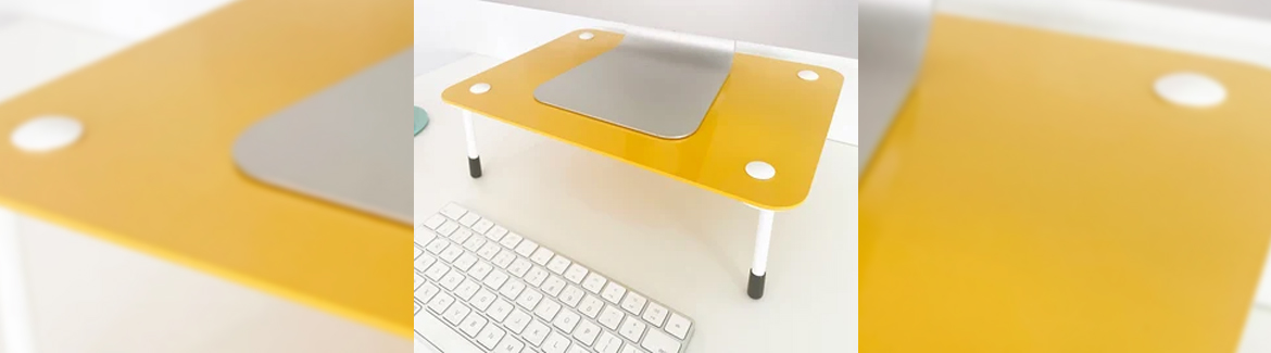 A iMac sits on a monitor riser with a yellow base and white legs.