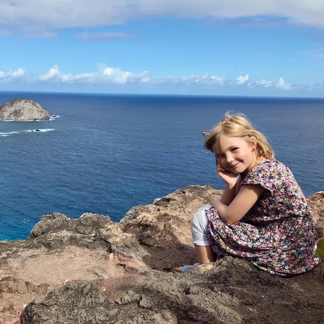 Penny's daughter Ella sits on a cliff in front of the ocean