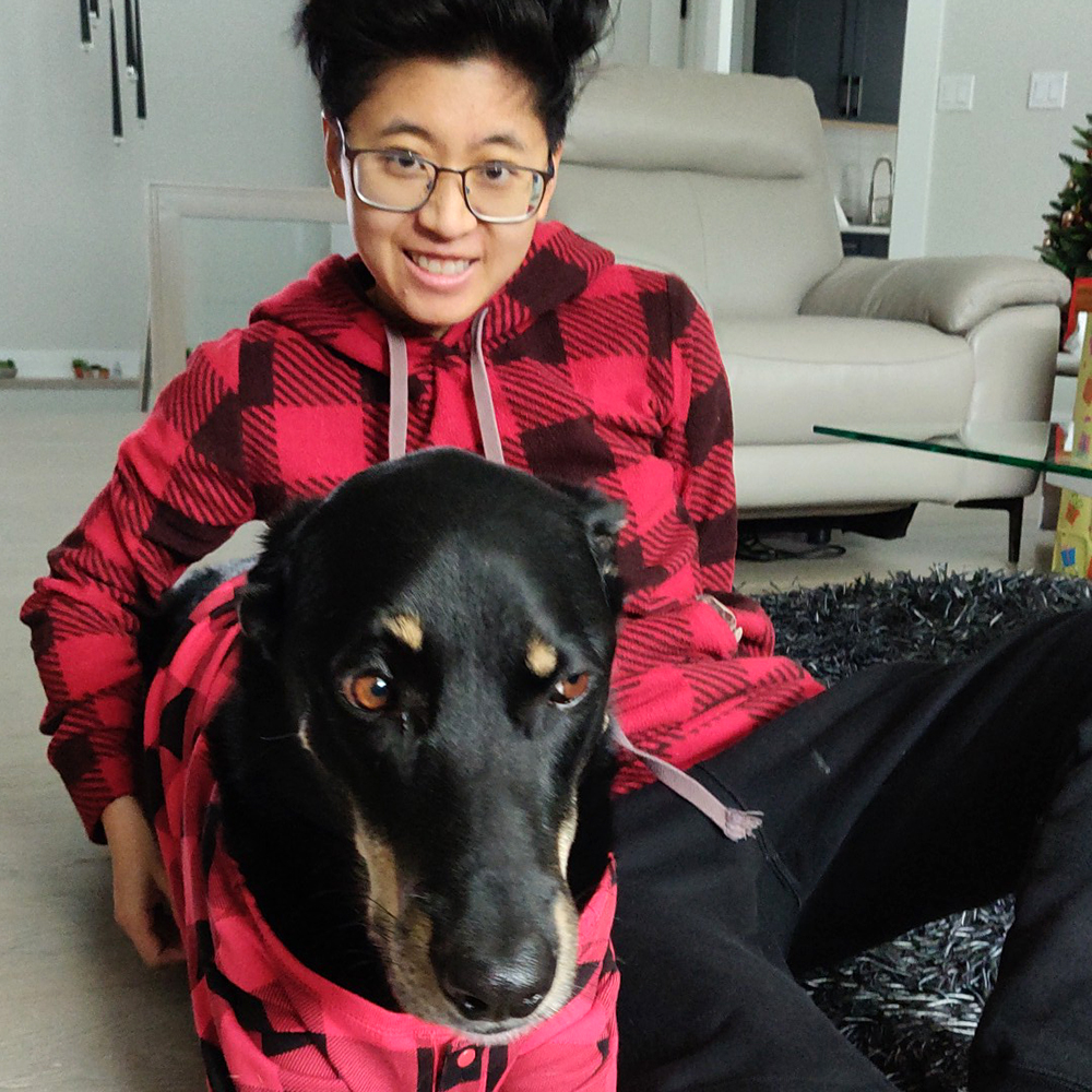 Renee and their dog, both wearing red and black plaid sweaters.