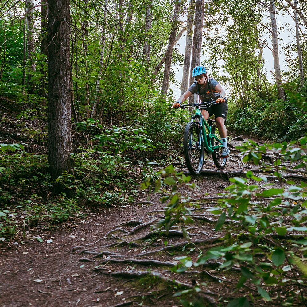 Emma rides her bike down a steep hill covered in tree roots