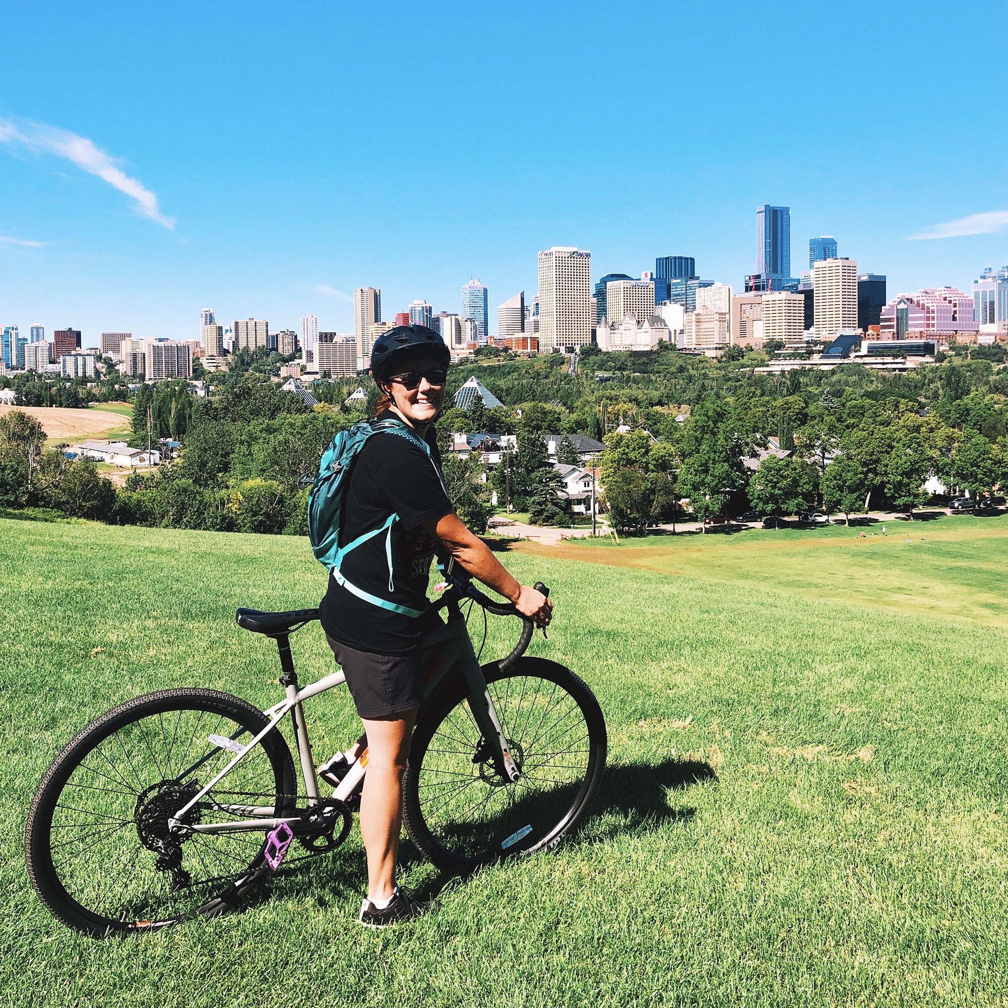 Jen posing on her bike in front of the Edmonton skyline