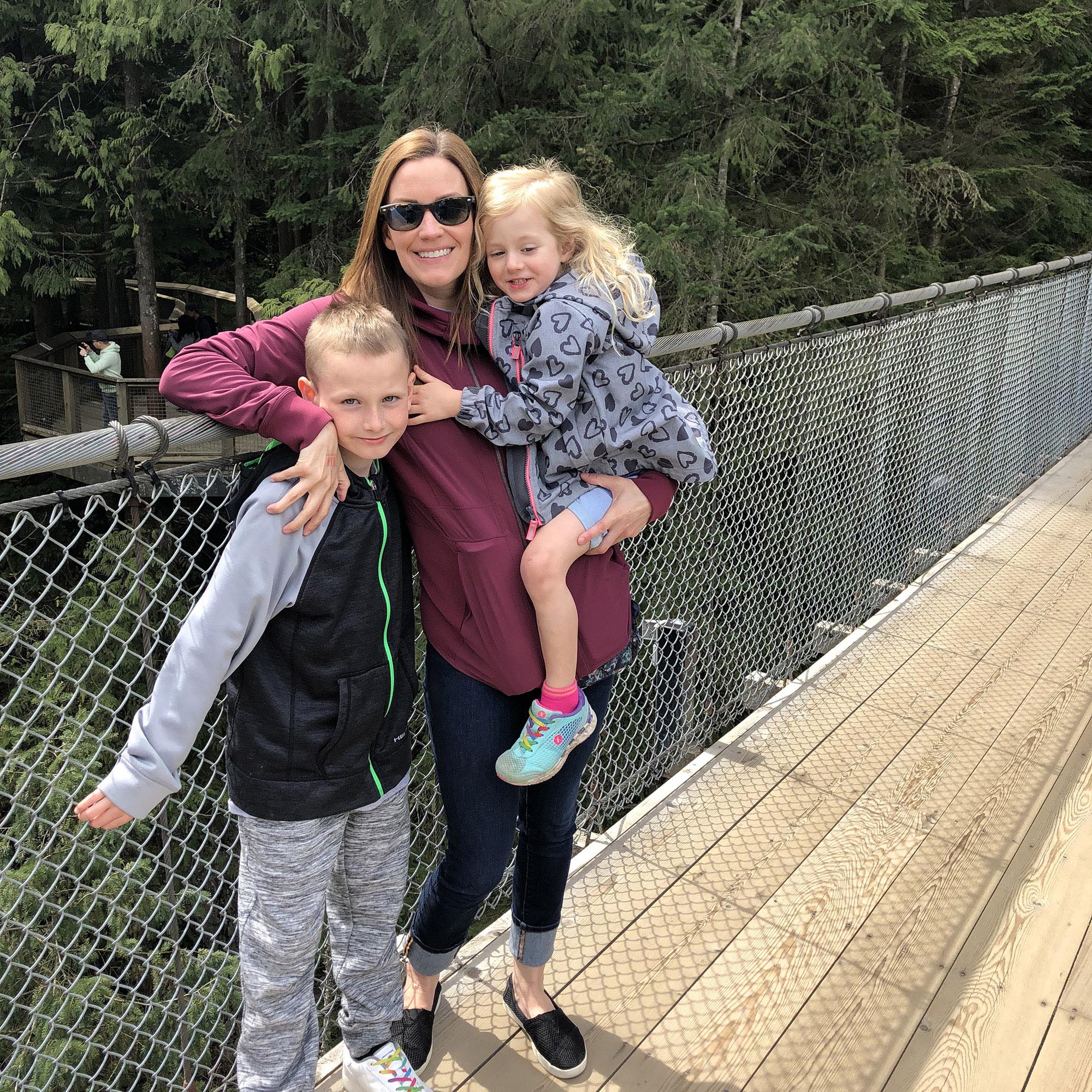 Sarah stands on a bridge while holding her niece. Her nephew is standing close beside them.