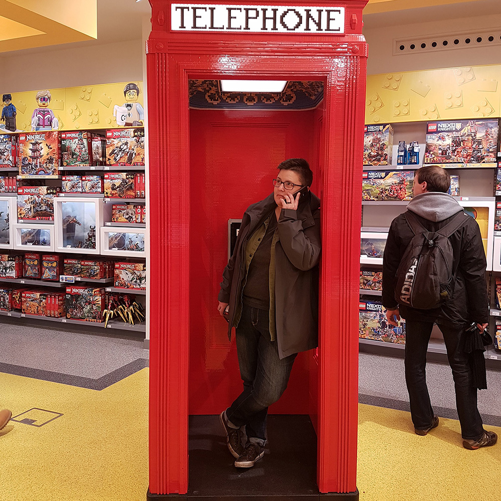 Dana talks on her phone in a red lego phone booth