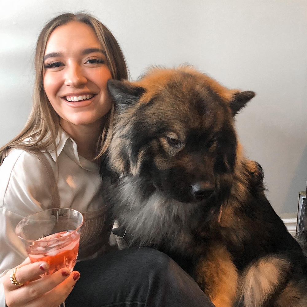 Kyra smiles while hugging her dog, Kylo. Kyra is holding a cocktail in her hand
