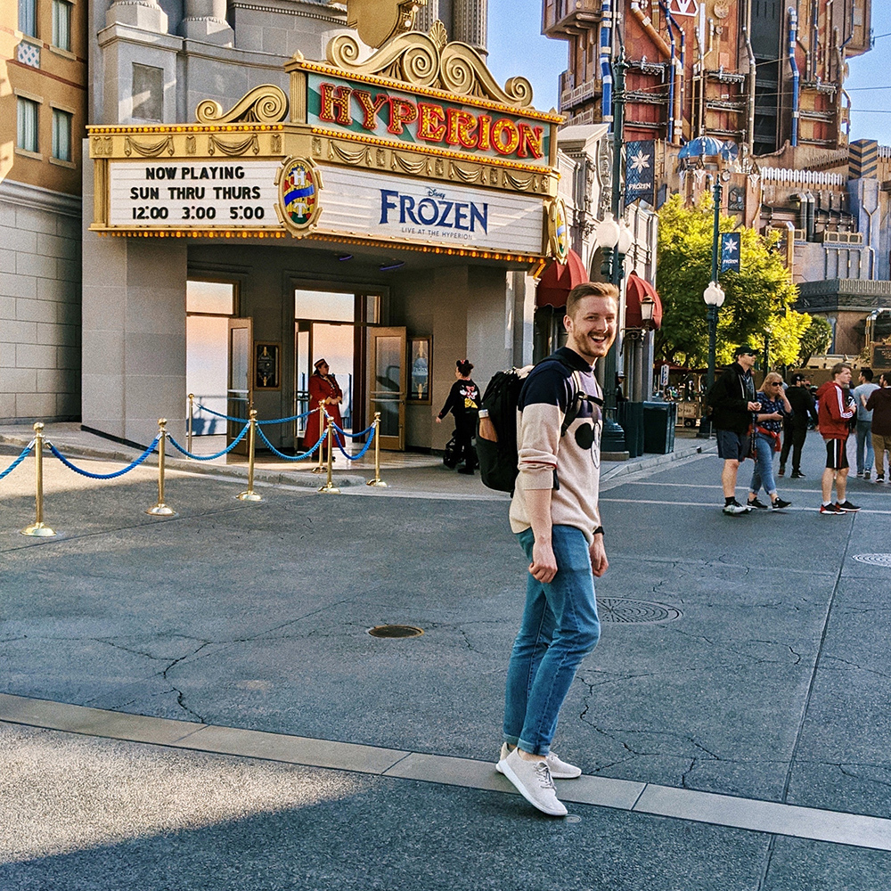 Matt smiles while standing in front of a theatre sign playing Disney's Frozen