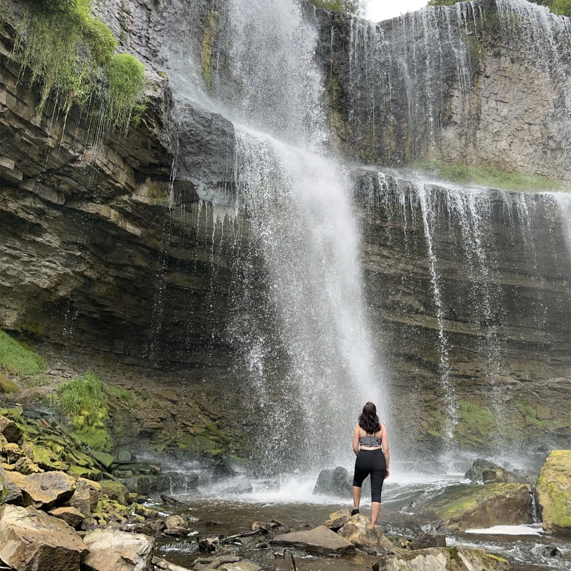 Jaime stands in front of a waterfall with her back to the camera
