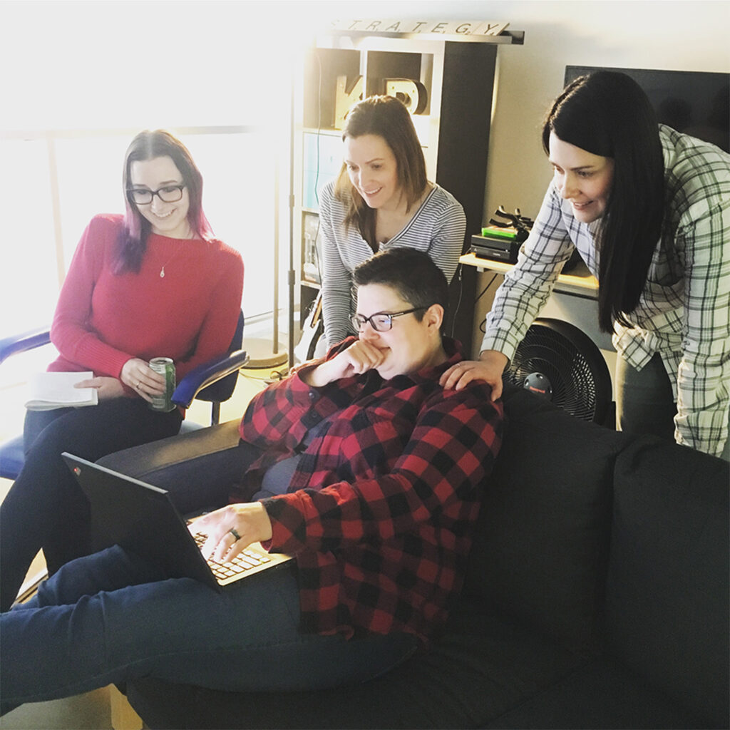 Brittany, Sarah, and Jen stand over Dana, all looking at her laptop