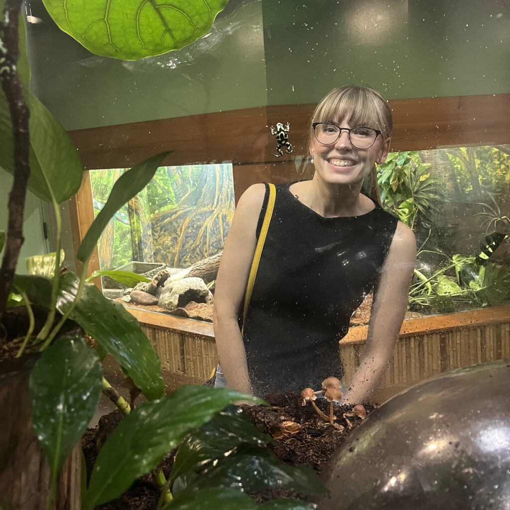 Liz behind a frog enclosure with a frog right by her face